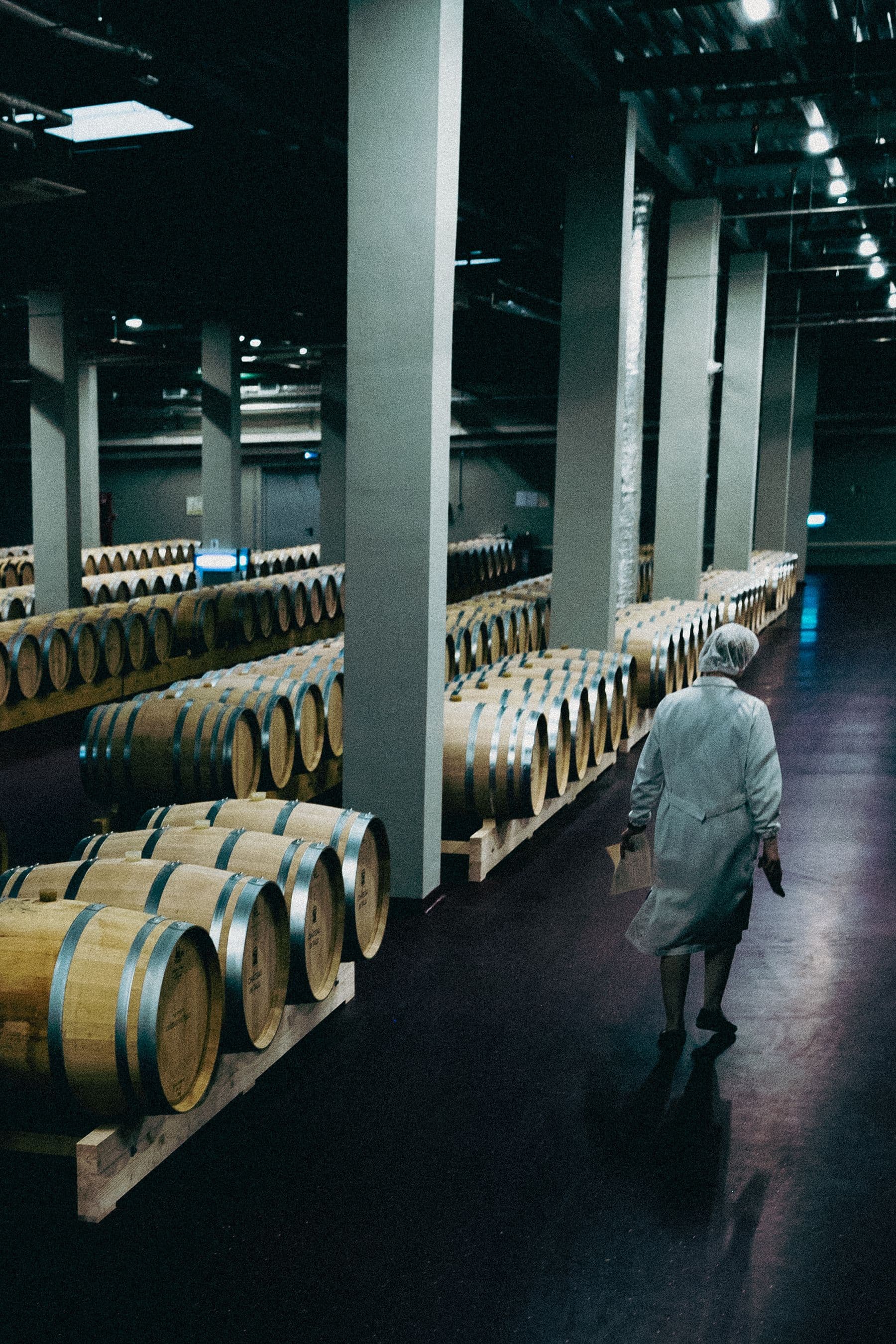 Worker walking between rows of barrels in a large wine cellar